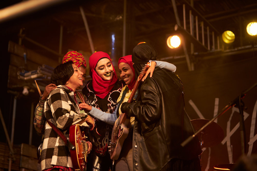 Bandmates all hug, smiling under the warm glow of concert lights